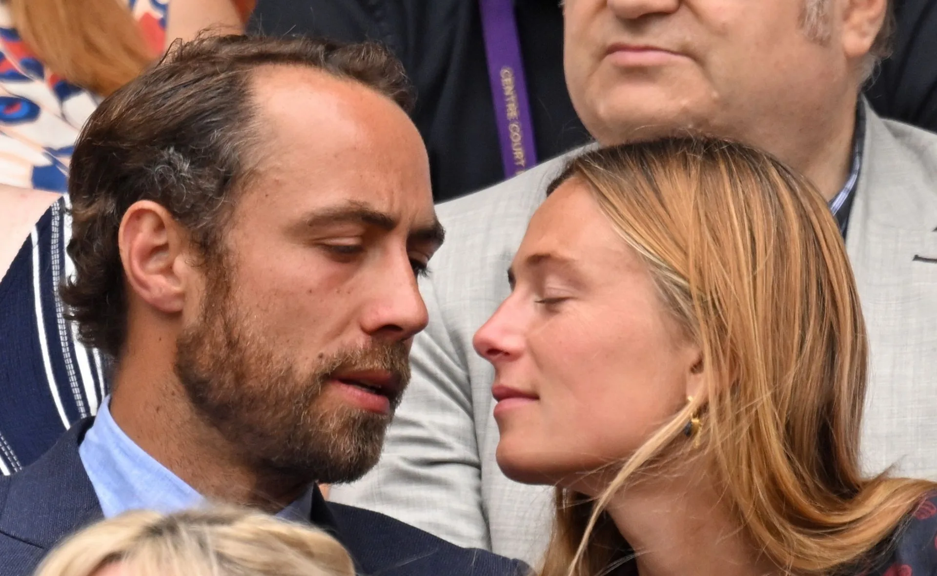 A couple gazing at each other closely at a formal event, surrounded by other attendees.