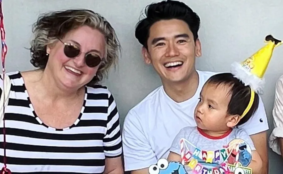 Three people smiling; a woman with sunglasses, a man, and a child wearing a birthday hat and holding a toy.