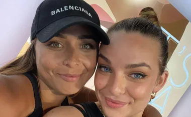 Two people smiling for a selfie; one wearing a hat.