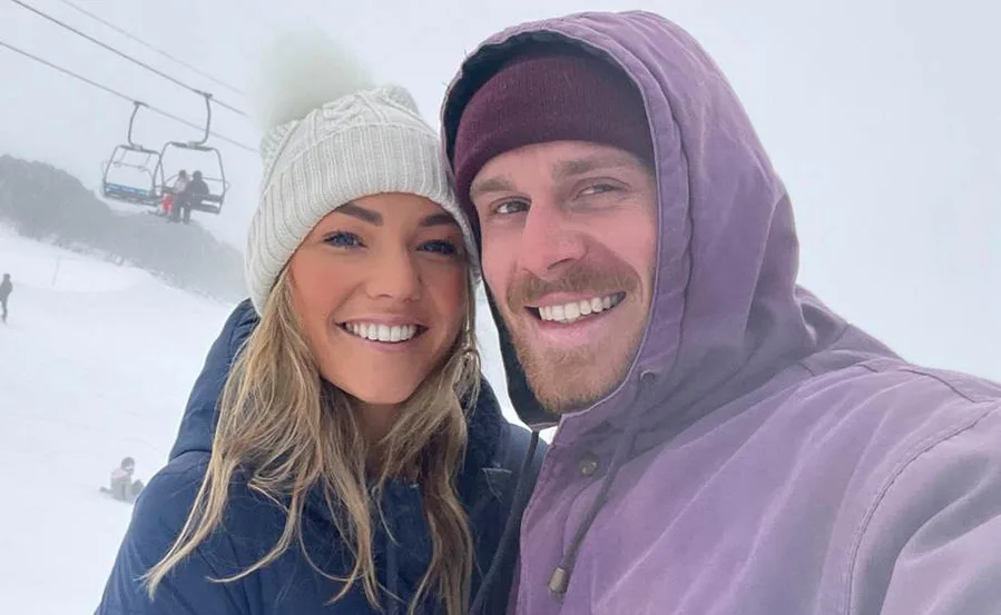 A couple smiling in winter clothes on a snowy mountain, near a ski lift.