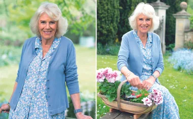 A woman in a blue floral dress smiles outdoors near plants and flowers.