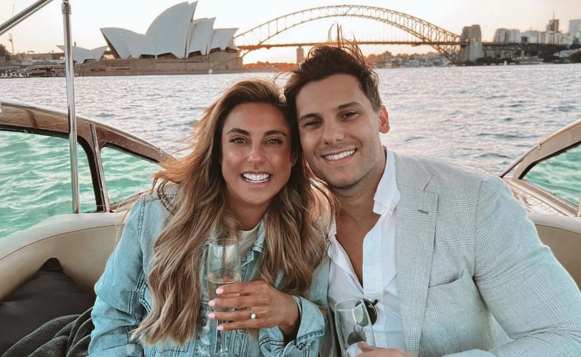 Couple smiling on a boat with Sydney Opera House and Harbour Bridge in the background, holding champagne glasses.