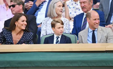 A family smiling and watching a tennis match at Wimbledon, seated in the stands.