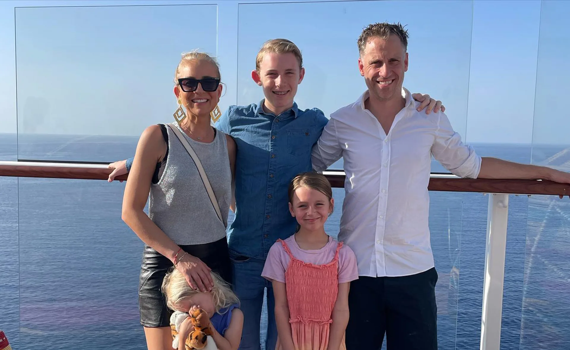 A family of five posing together on a cruise ship deck, with ocean in the background.