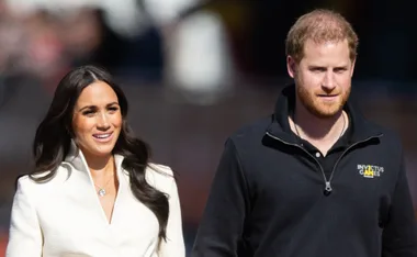 Prince Harry and Meghan Markle walking outdoors, with Harry wearing an Invictus Games jacket.