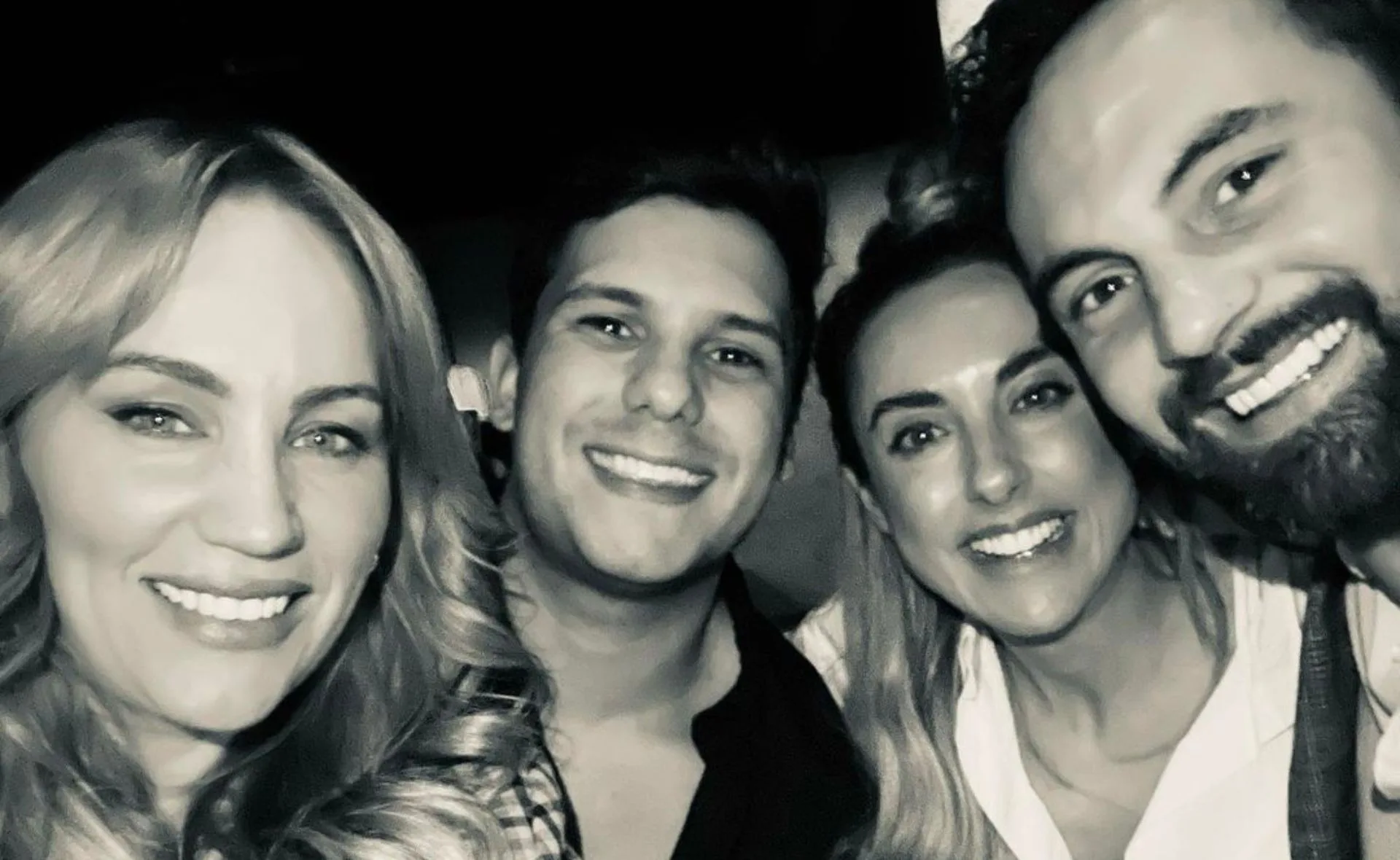 Four people smiling closely together in a black and white photo.