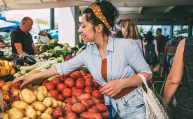 Woman shopping for fresh produce at a market, selecting tomatoes and potatoes.