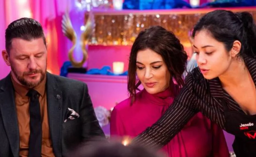 Three people in a colorful room, one serving food, with pink and blue decor in the background.