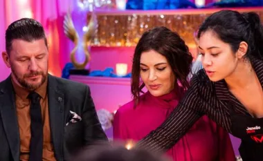 Three people in a colorful room, one serving food, with pink and blue decor in the background.