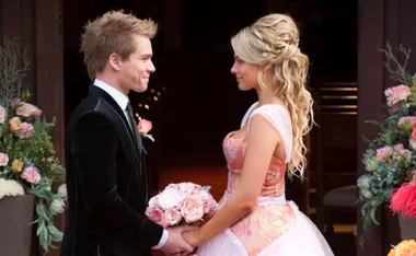 A bride and groom hold hands, facing each other, surrounded by floral arrangements.