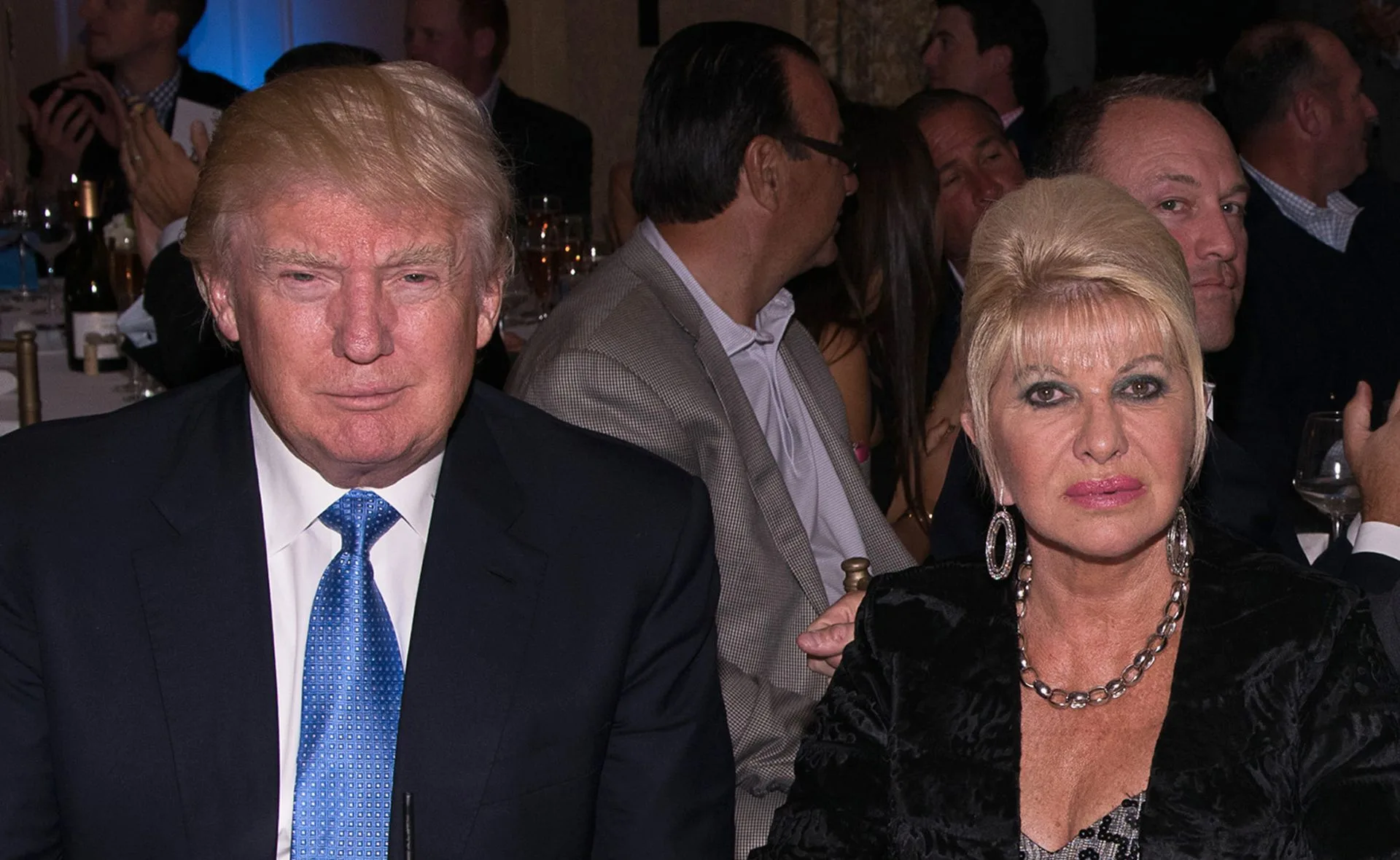 A man in a suit and a woman in a black outfit sitting at a formal event.