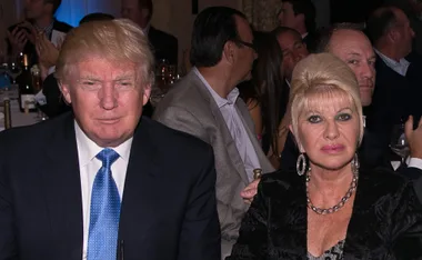 A man in a suit and a woman in a black outfit sitting at a formal event.