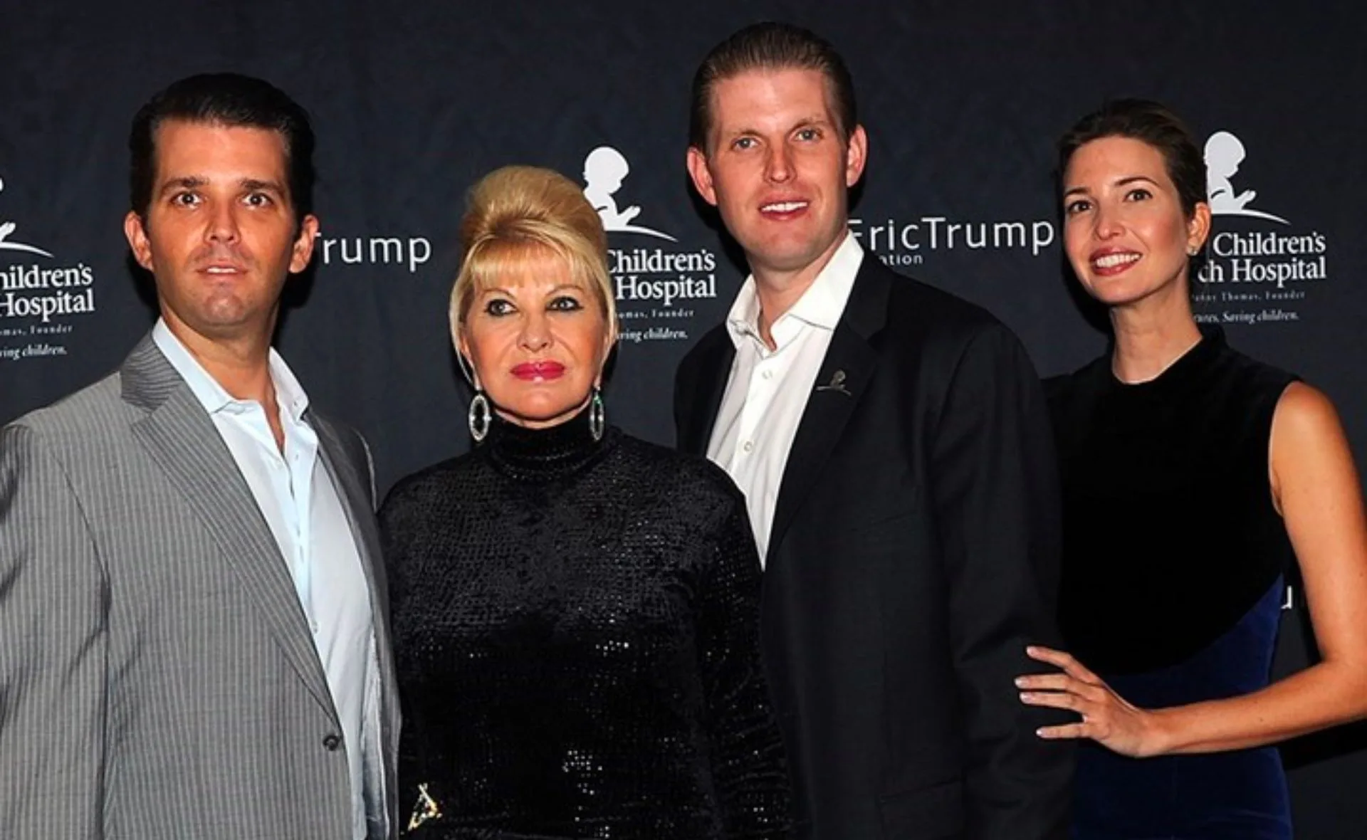 A group of four individuals posing together at a charity event backdrop.