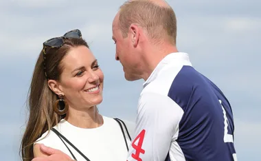 Man and woman smiling at each other, embracing outdoors under a clear sky.