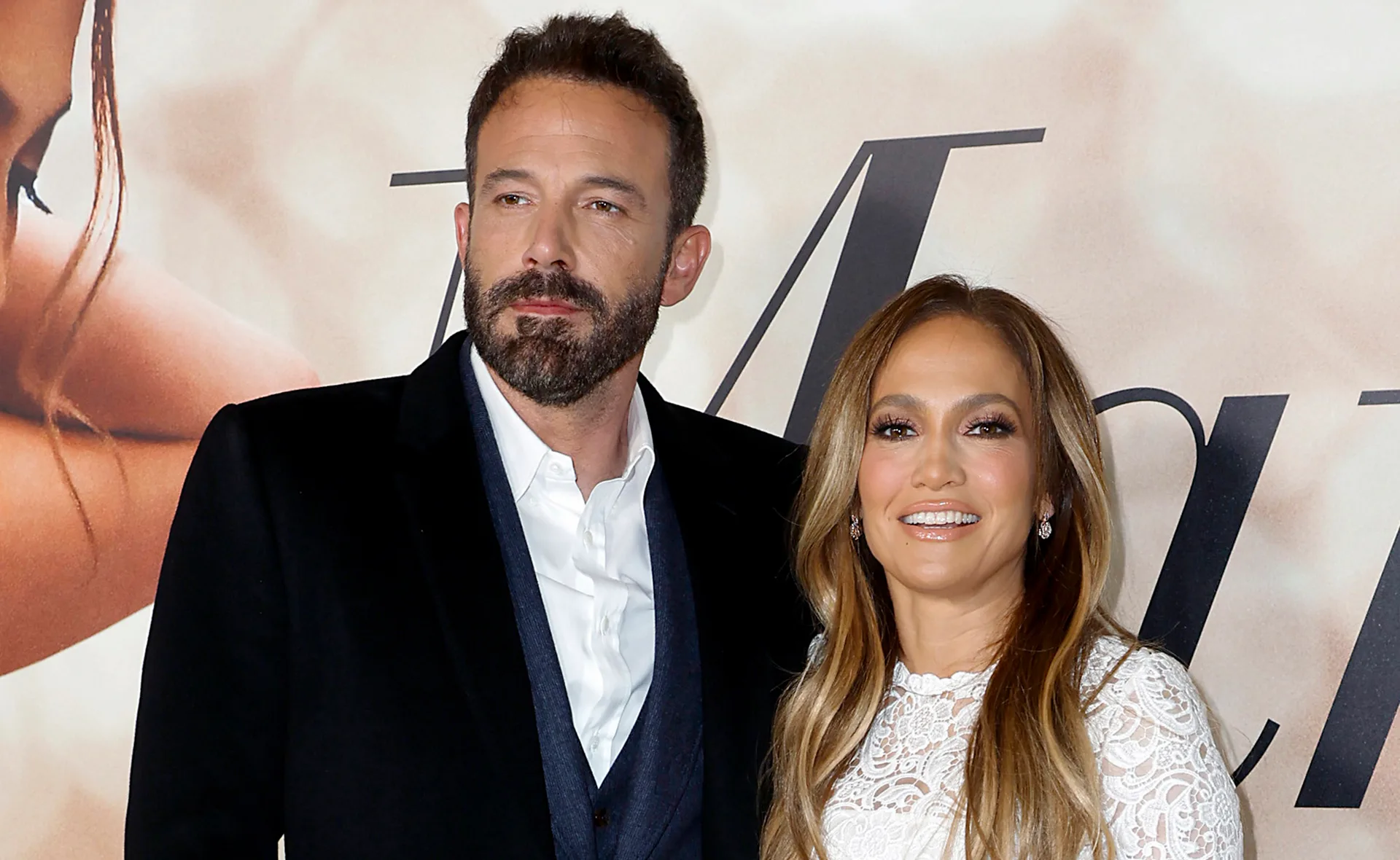 A couple on the red carpet, both dressed formally, smiling at an event backdrop.