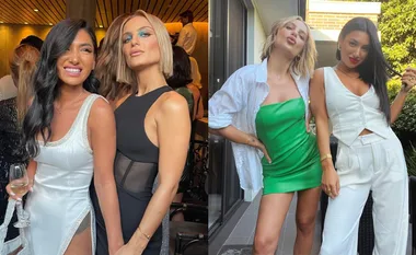Two women posing together at an event, smiling and dressed stylishly, one in white and the other in black and green.