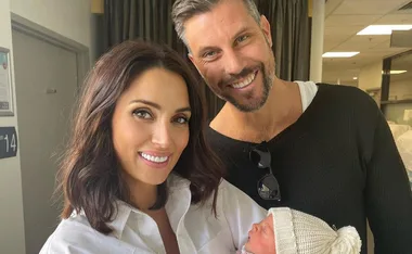 A woman and man smiling, holding a newborn baby, in a hospital setting.