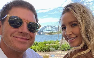 Two people smiling with Sydney Harbour Bridge in the background on a sunny day.