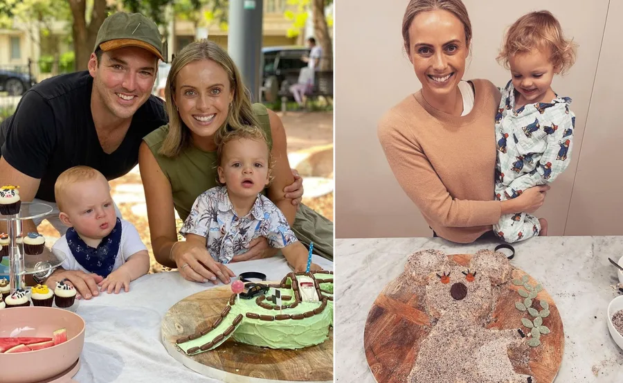 A smiling family enjoys time together; woman holds toddler, next to a creative cake on a table.