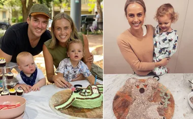 A smiling family enjoys time together; woman holds toddler, next to a creative cake on a table.