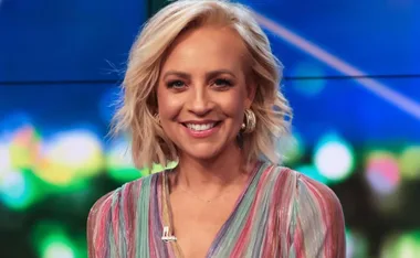 Smiling woman with short blonde hair, wearing a colorful striped top and hoop earrings, on a blurred colorful background.