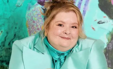 Woman smiling, wearing a turquoise jacket, against a colorful abstract background.