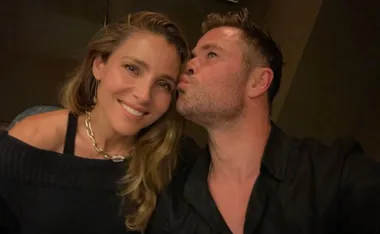 Man kissing a woman on the cheek, both smiling, in a dark setting.