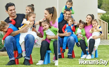 Family with four toddlers in colorful outfits smiling and playing outside on the grass, celebrating a birthday.