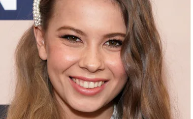 Smiling person with long wavy hair, wearing a pearl hair accessory.