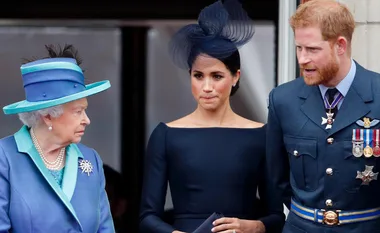 Three people standing on a balcony, two in formal attire and one military, attending an event.