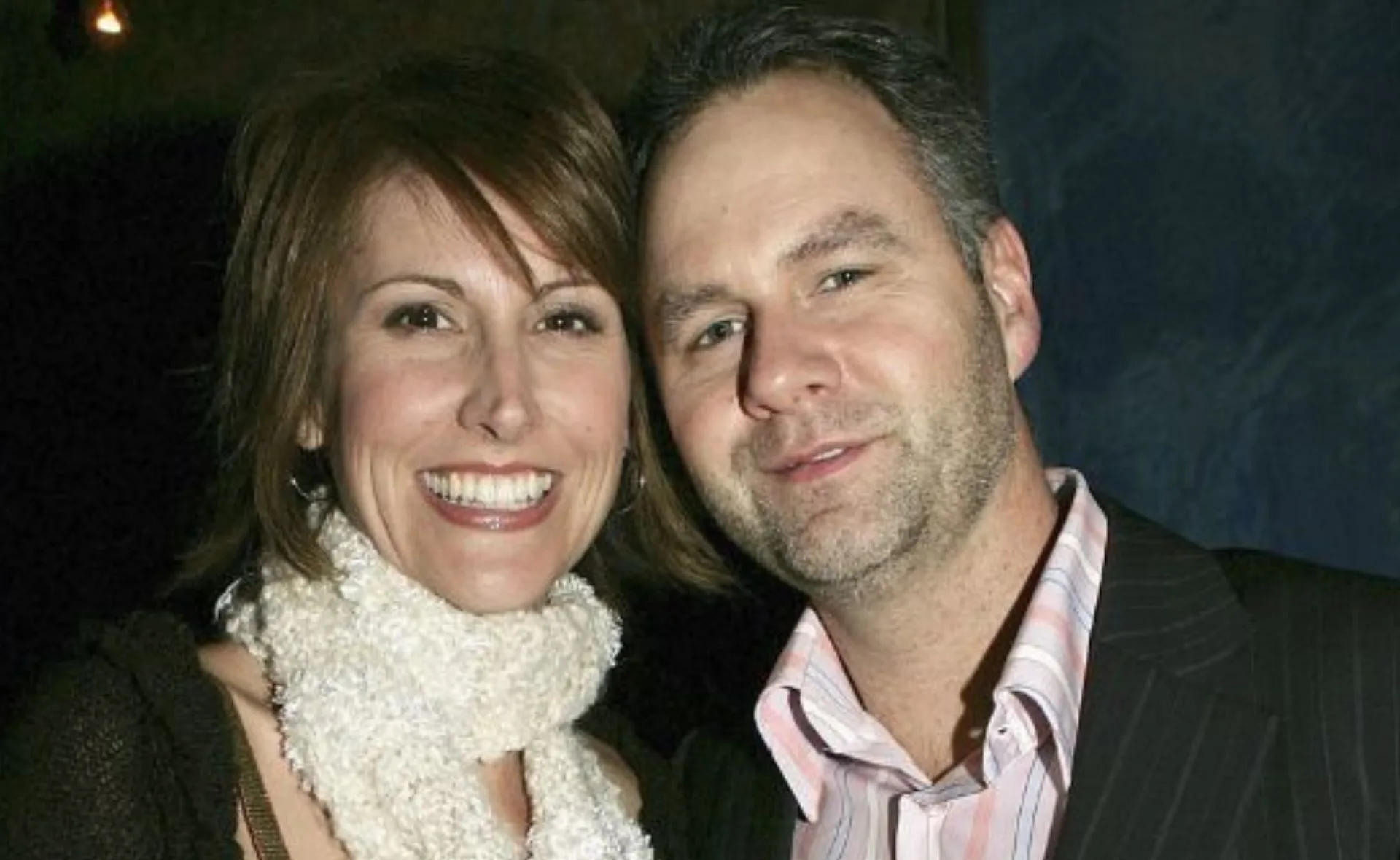 A woman wearing a scarf smiles beside a man in a suit.