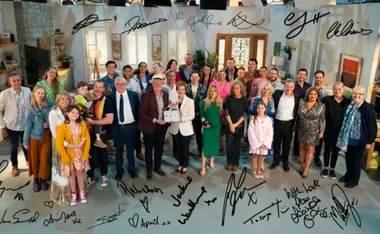 "Neighbours cast and crew posing on set with autographs of actors overlaying the image."