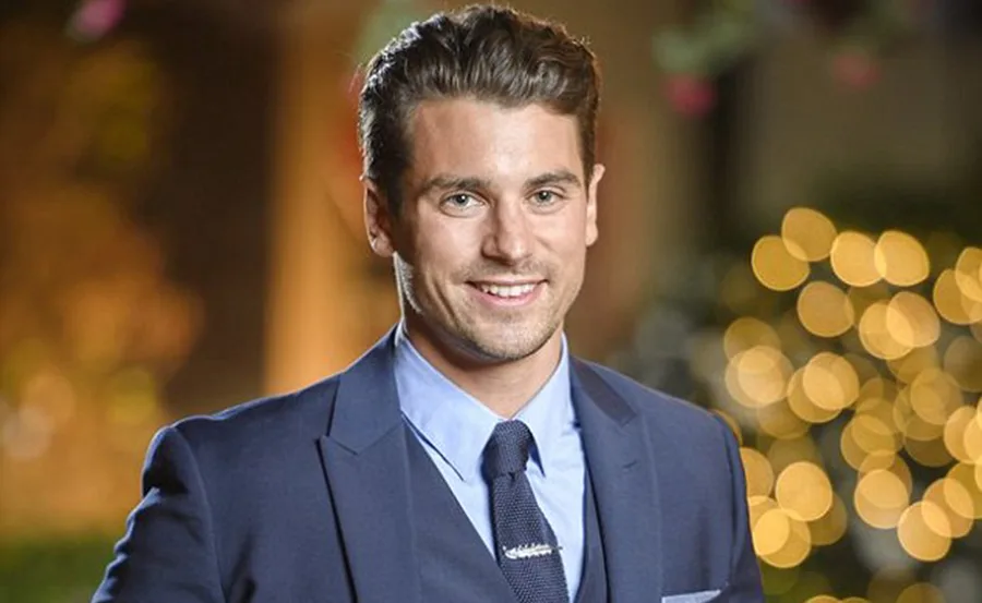 Portrait of a smiling man in a dark suit with blurred lights in the background.