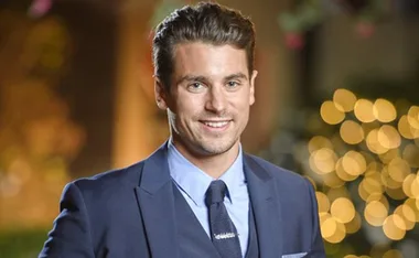 Portrait of a smiling man in a dark suit with blurred lights in the background.