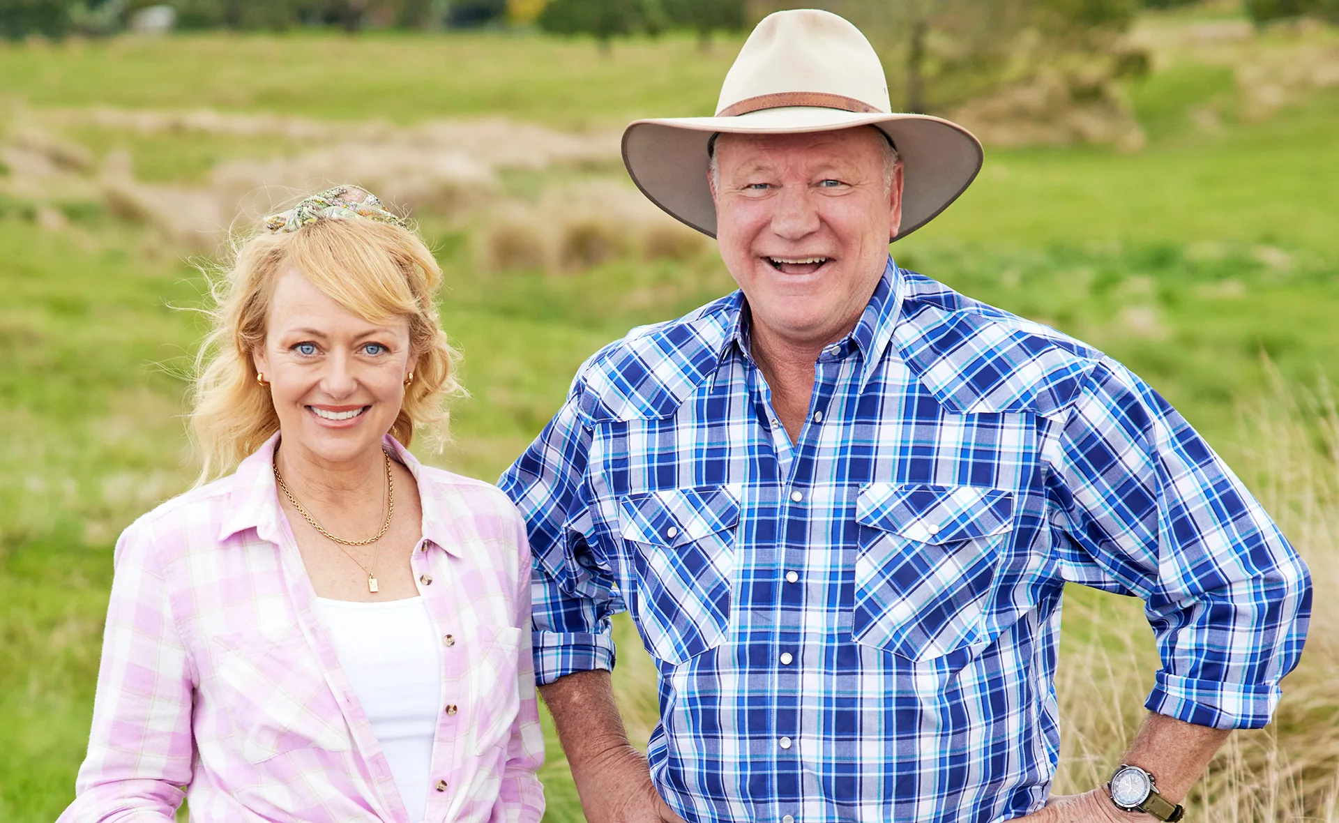 A man and woman in plaid shirts smiling in a grassy field.