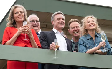 Five people on a balcony smiling and holding champagne glasses during a celebration.