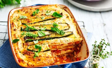 Vegetable lasagne with grilled zucchini and fresh basil in a blue baking dish on a wooden table.