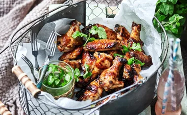 Grilled chicken wings garnished with cilantro in a basket, with forks and a jar of extra cilantro on the side.