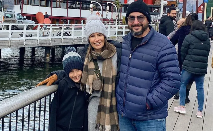 Family in winter clothes smiling by a waterfront with a docked boat in the background.