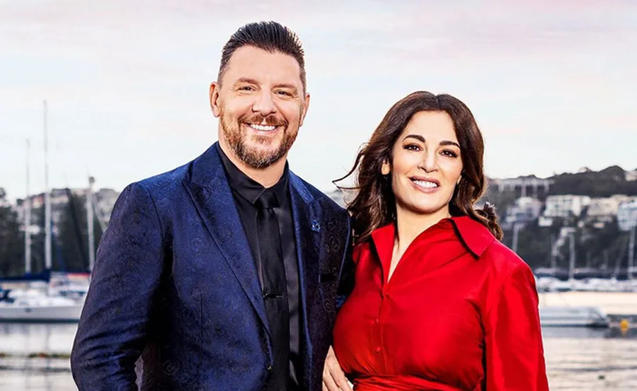 A man in a blue suit and a woman in a red dress smiling in front of a marina backdrop.
