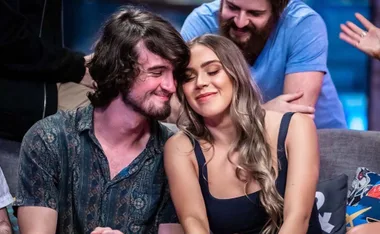 A couple sitting close on a couch, smiling affectionately, with two people in the background.