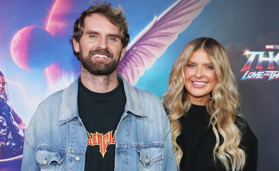 A smiling couple poses in front of a "Thor: Love and Thunder" movie poster backdrop.