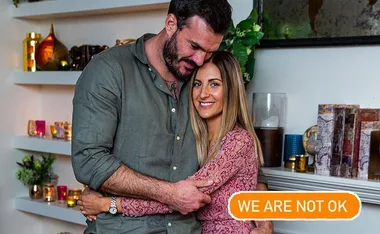 Couple embracing warmly in a cozy room with the text "WE ARE NOT OK" displayed.