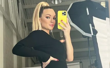 Person taking a mirror selfie with a yellow phone, wearing a black outfit and a high ponytail.