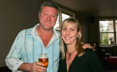 Man and woman smiling indoors; man holding a beer, woman in a black top.