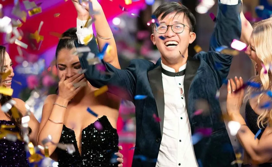 Celebratory scene with people in formal attire, colorful confetti falling, a man raising his hand joyfully.