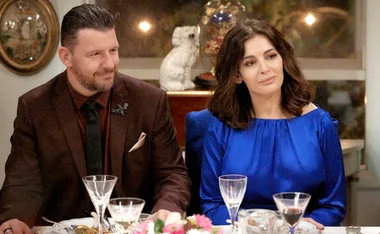 A man and a woman sitting at a dinner table with elegant glassware, appearing thoughtful and content.