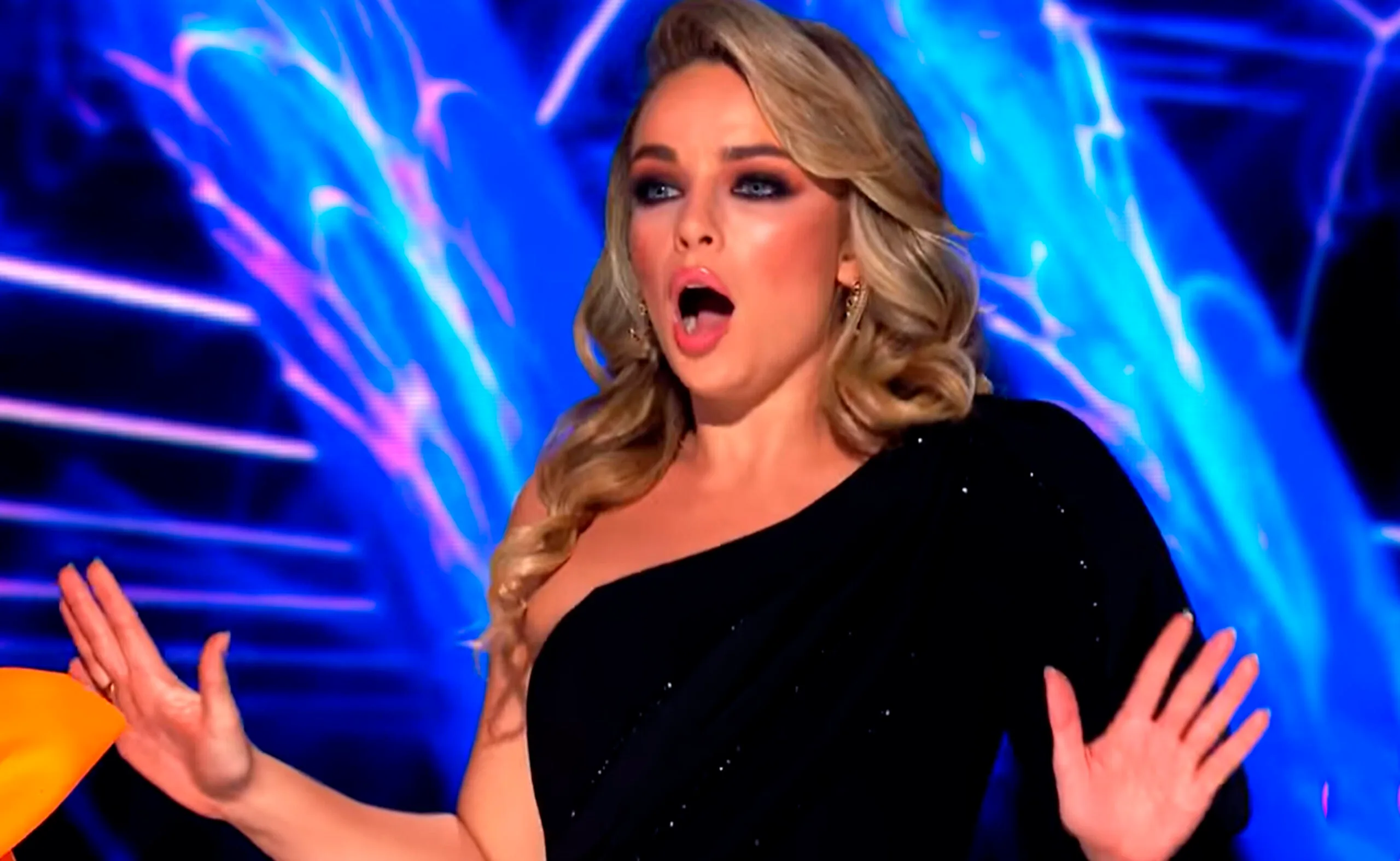 Woman in a black dress expresses shock; colorful background on "The Masked Singer."