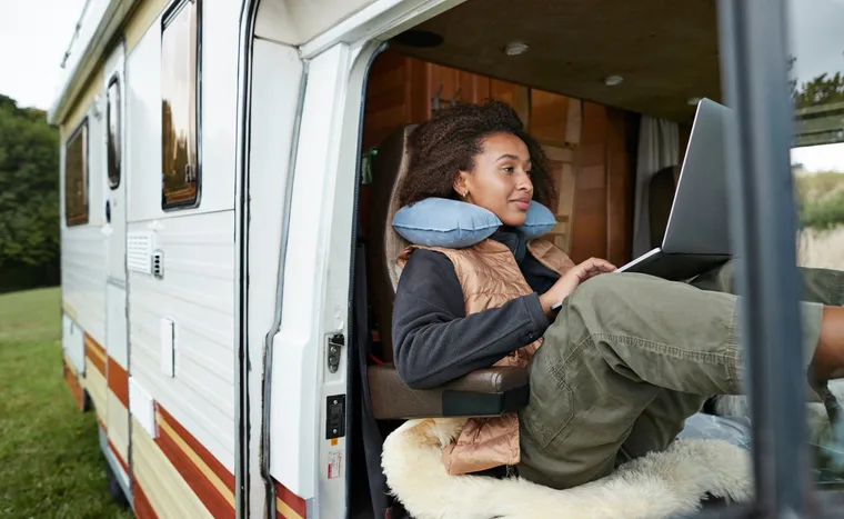 Person in a camper van using a laptop with a travel neck pillow for comfort.
