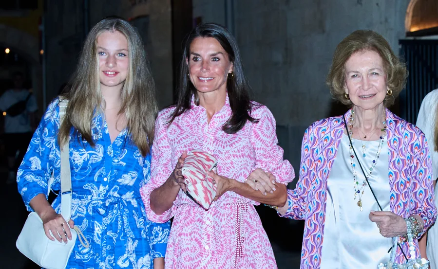 Three women in colorful dresses smiling at an evening event, one in pink and two in blue patterns.
